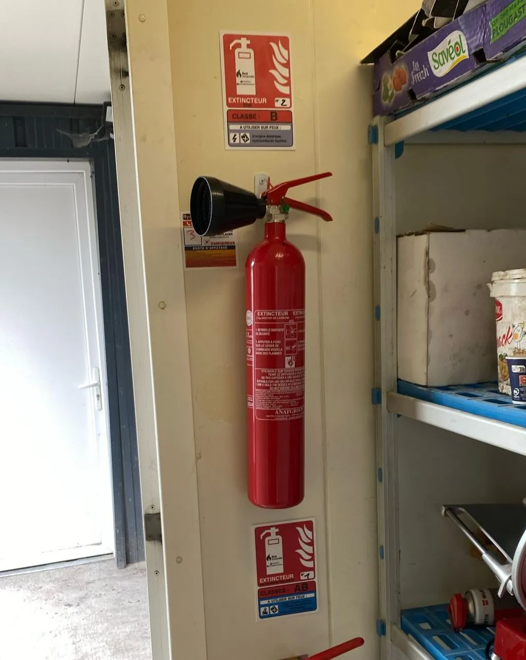 Extincteur CO2 de 2 kg accroché au mur, avec son tromblon noir, et au-dessus un panneau Extincteur CO2, classe B